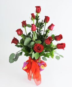 A dozen red roses arrive designed in a glass vase with lush foliage,