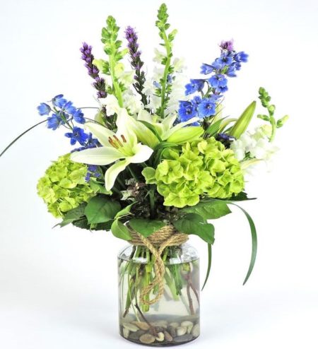 Sweet scented Casablanca lilies surrounded by green hydrangeas and additional wildflowers in a decorative modern vase with rope handle.